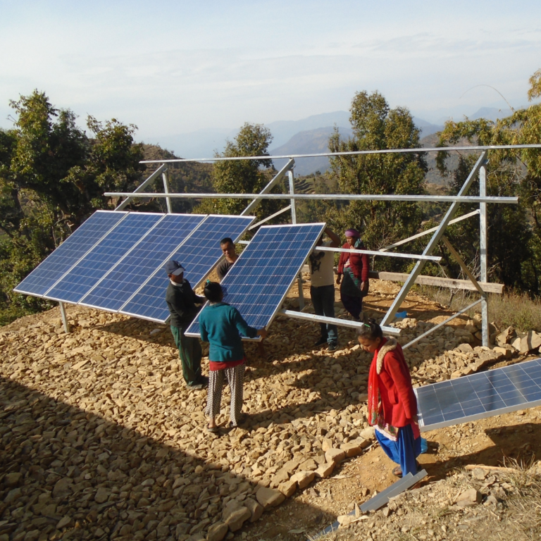 Three men are carrying solar panels, lifting them onto a large metal structure where they will be secured. Three panels have already been put in place.