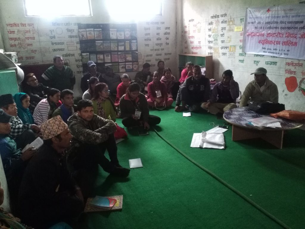 Community members sat on the ground in a room receiving training