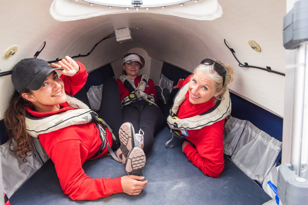 Three members of All Systems row lying down in the boat's sleeping quarters (there's not much room in there!)