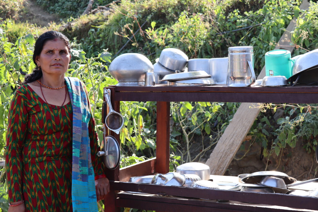 A Nepali woman standing outside next to her wooden dish drying rack