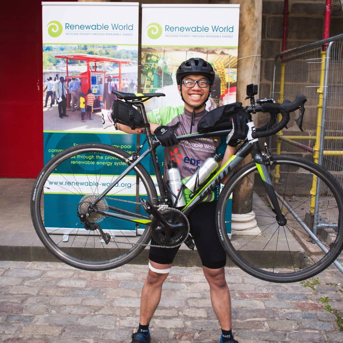 Cyclist standing in front of banners holding up a bicycle